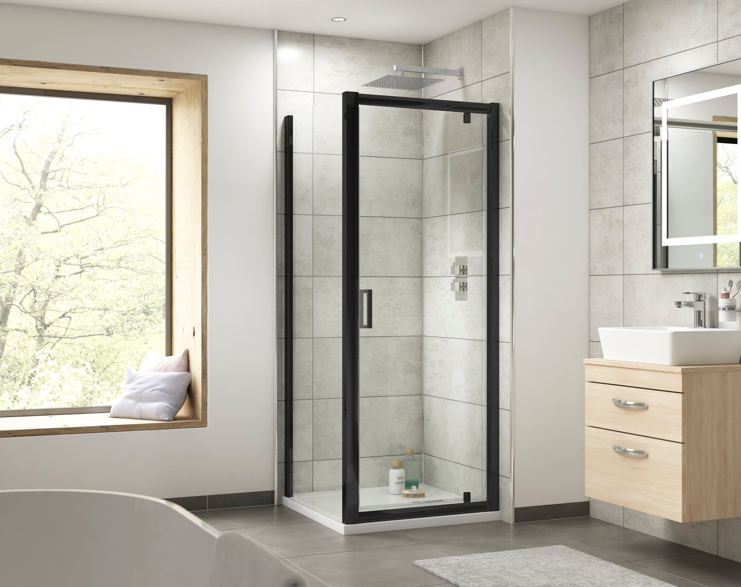Image shows a matt black framed sliding shower door with clear glass panel enclosure and a square D-bar handle. Featuring light stone tiles and light wooden vanity unit with square white countertop basin and chrome tap.