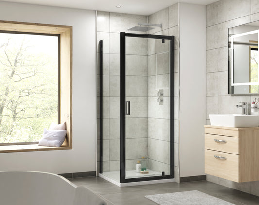 Image shows a matt black framed sliding shower door with clear glass panel enclosure and a square D-bar handle. Featuring light stone tiles and light wooden vanity unit with square white countertop basin and chrome tap.