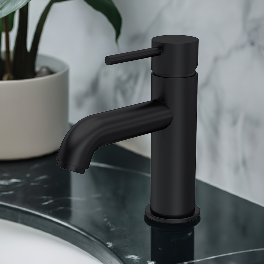A black mono basin mixer tap with a push button waste, set against a marble background with a plant to the side.